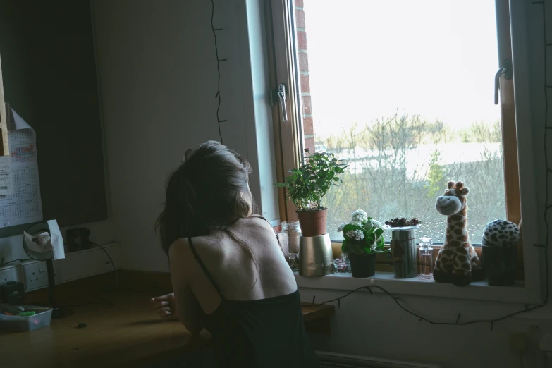 a girl looking out a window with a giraffe toy in the background