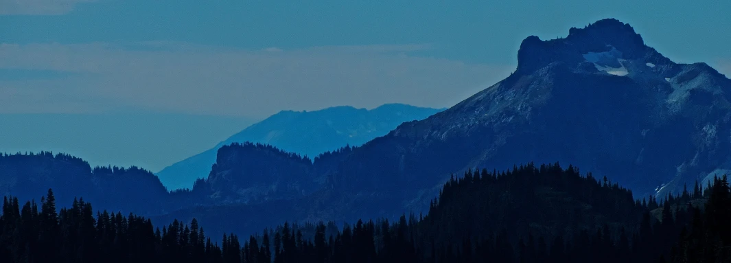 a mountain view in the evening, with trees and blue skies