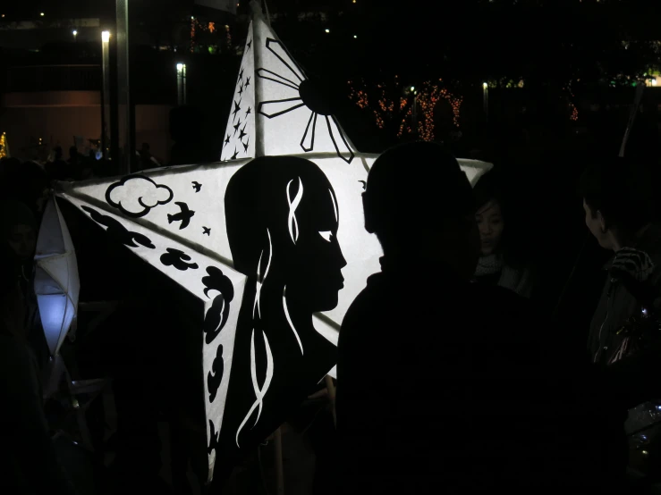 a large kite is displayed with a person's image and lights in the background