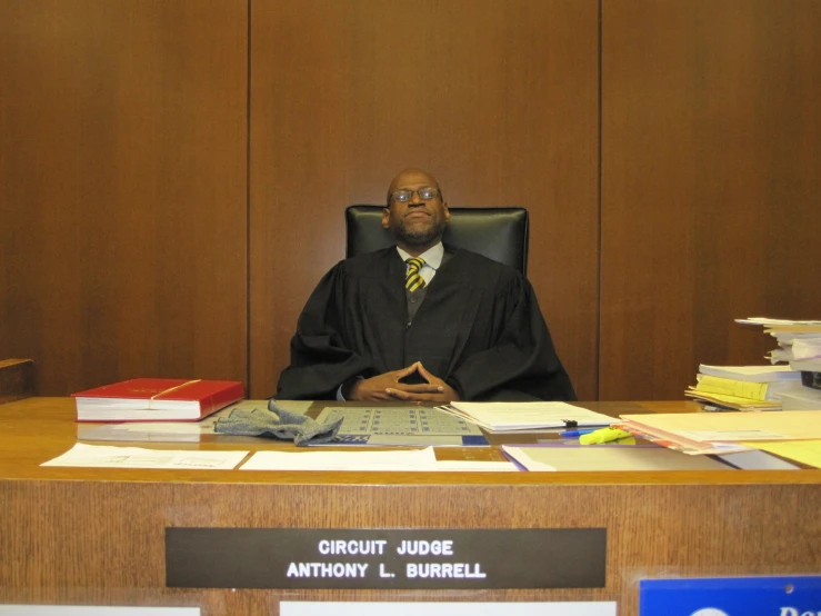 the judge sits at his desk with papers and a computer