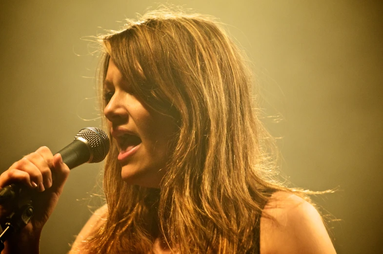 a woman is singing into a microphone with bright light in the background