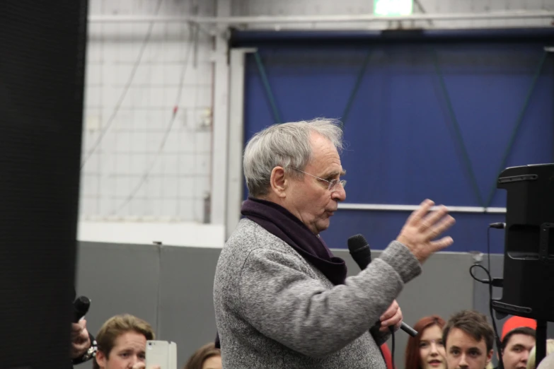 an older man speaking at a podium surrounded by people