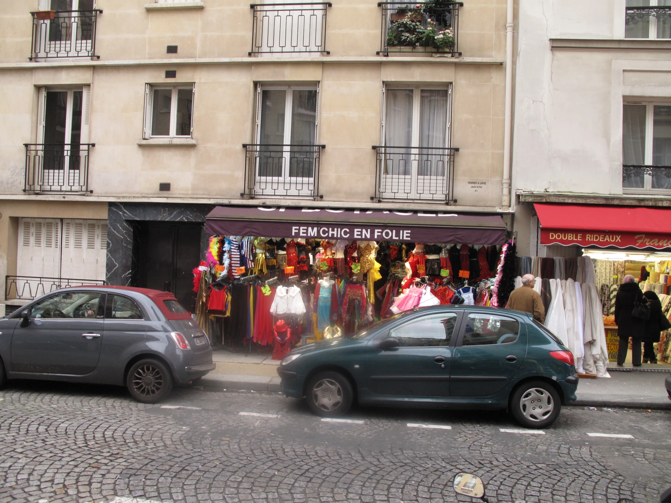 cars are driving down a street with people standing and shops