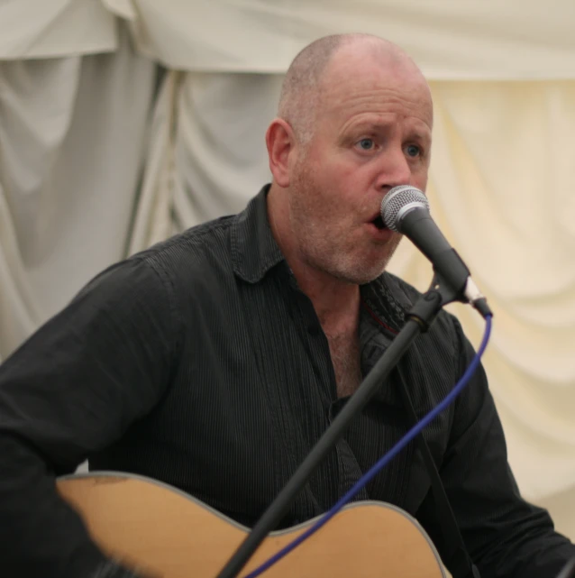 a bald headed man holding a guitar playing