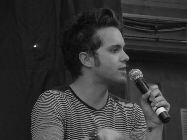 a man with long hair sitting down while holding a microphone