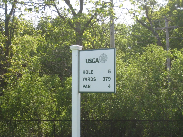 a white sign is on a pole next to the trees