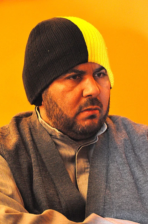 a man with a beard and a knit hat sits next to a bright wall