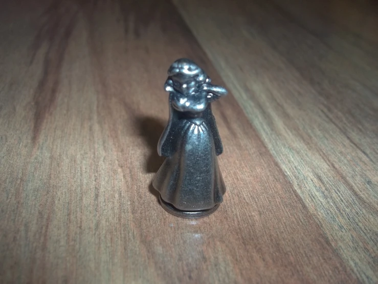 a toy on a wooden surface has a white coat and silver hat