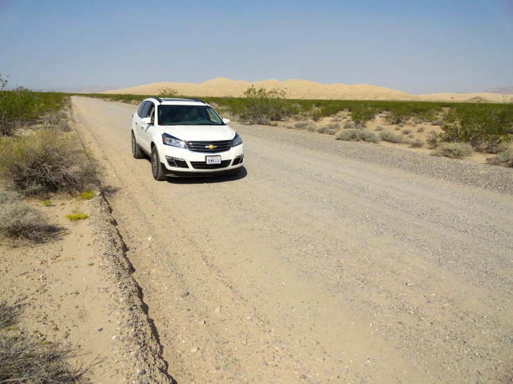 white car parked on dirt road next to dry grass