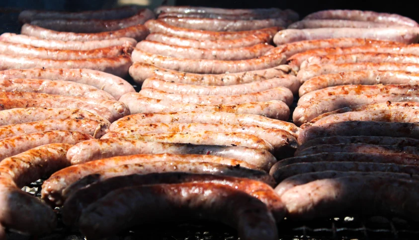 a lot of sausages being grilled on the grill