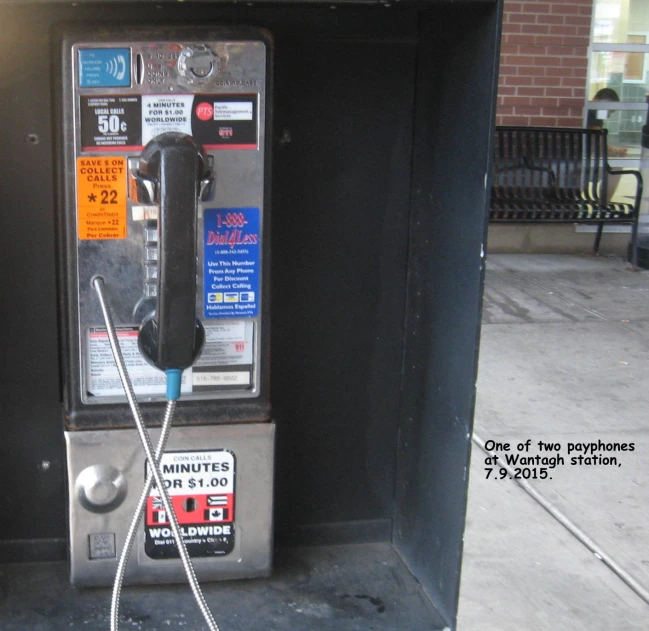 a pay phone stands on a sidewalk next to a pole