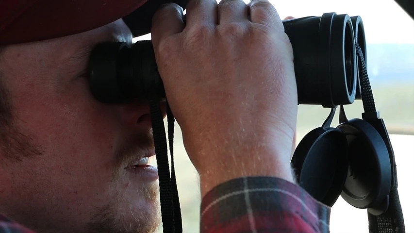 the man in a red cap looks through binoculars