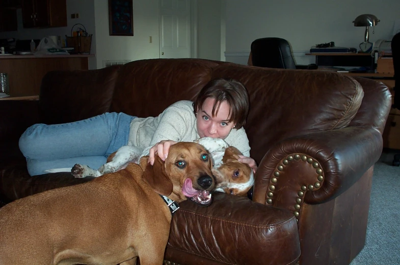 a woman cuddles with two dogs on the couch
