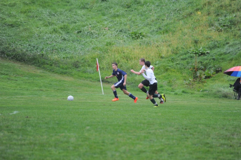 some boys playing soccer on a hill with one person holding an umbrella