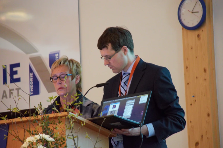 a woman holding a laptop in front of a man