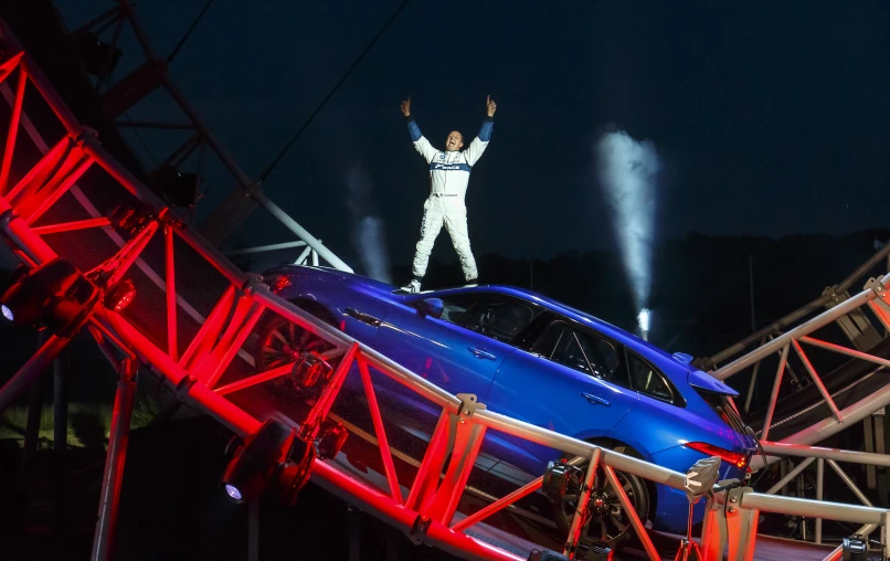 a person standing on top of a blue car in front of some lights