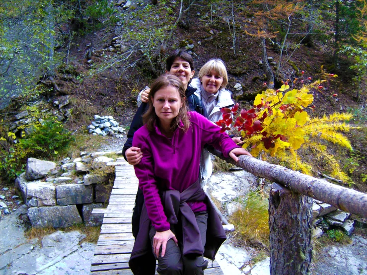 three women posing on a walkway near a wooded area