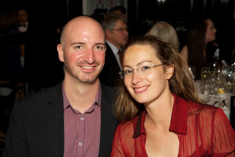 two people smile at the camera with a crowd of people in the background