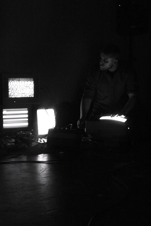 two people sit in the dark, in front of multiple tv monitors