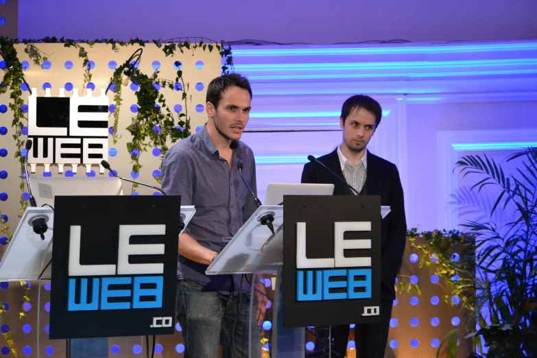 a man looking at a laptop in front of another on stage