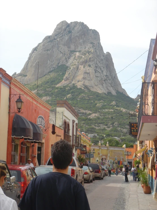 a busy street with cars parked near tall buildings and a large mountain in the background