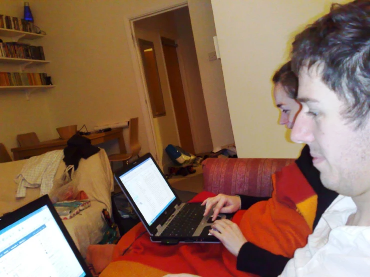 man in an orange and black sweater sitting on couch with laptops