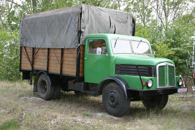 a green truck with a canvas covering is parked in some grass