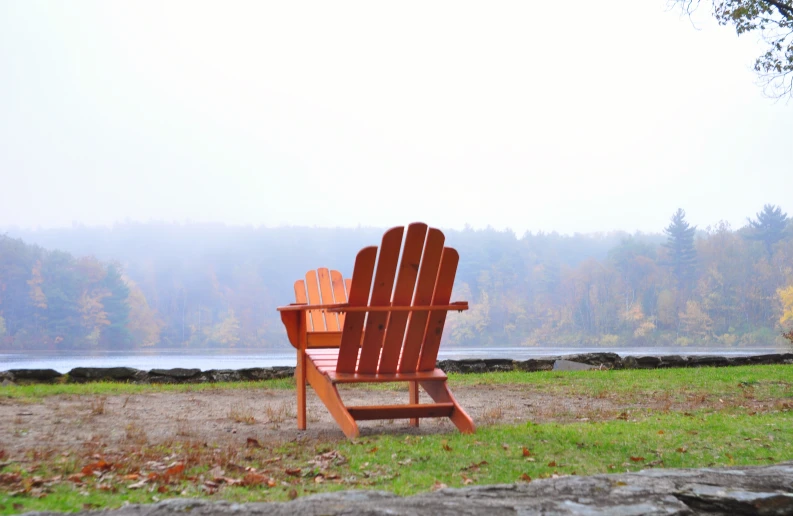 a wooden lawn chair near a pond on a foggy day