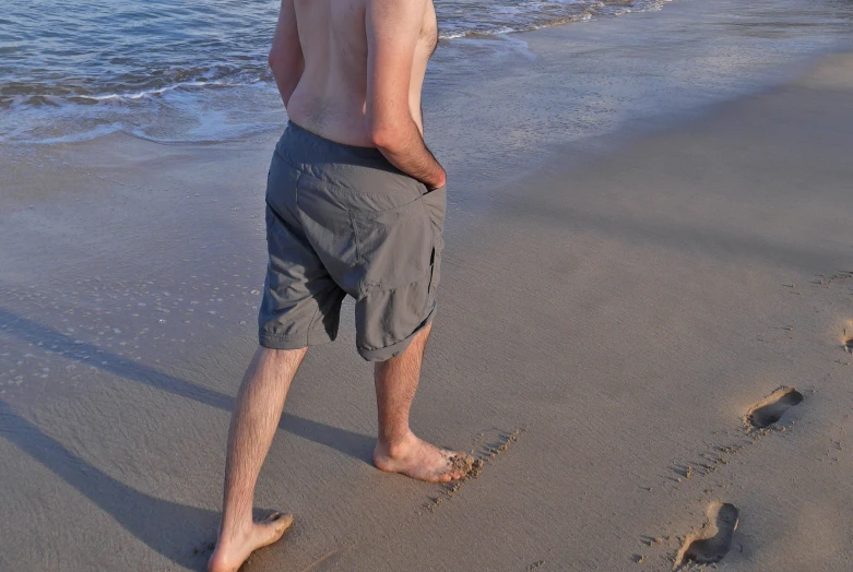 shirtless man walking on the beach near the ocean