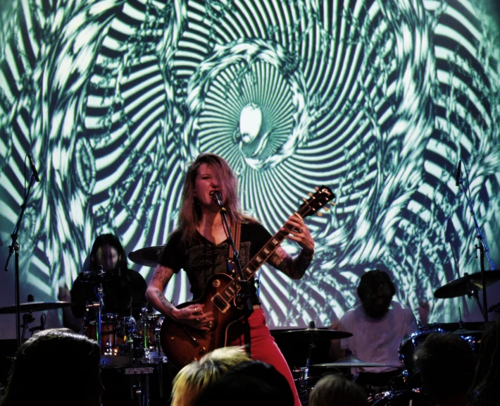 a woman standing in front of a projection of swirling swirls playing guitar