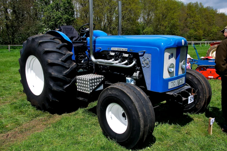 a man in brown shirt standing next to blue tractor