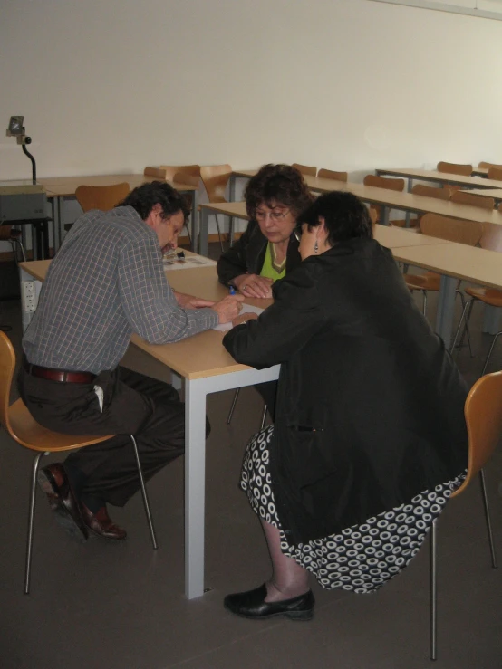 three people sitting at a table and one is playing checkers