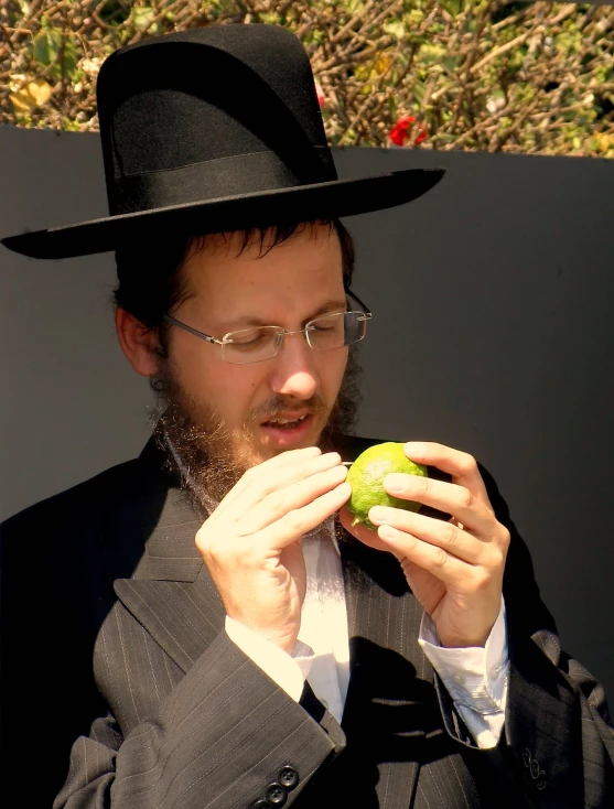 a man with glasses is wearing a top hat and holds a apple in his hands