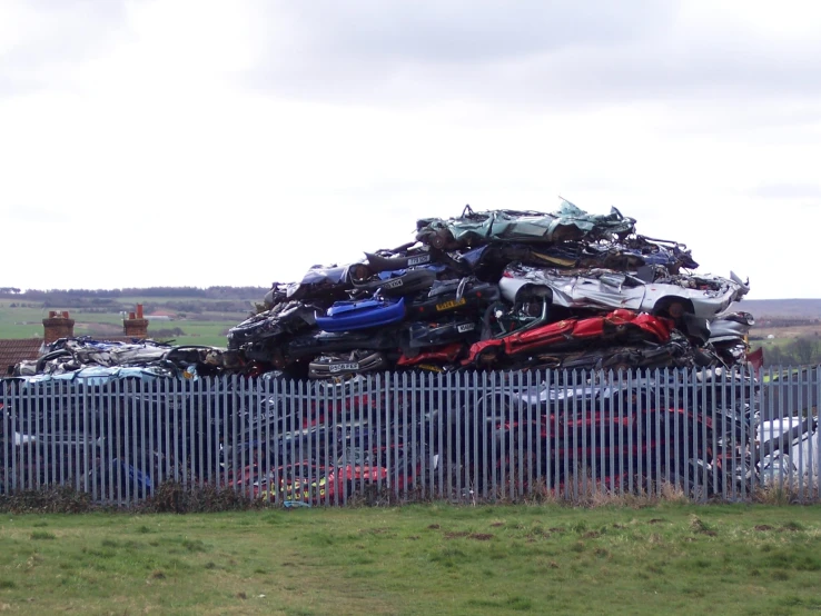 some cars stacked on top of each other in front of a fence