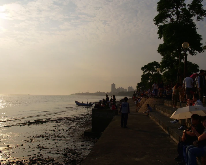 people sitting and walking along a lake shore as the sun sets