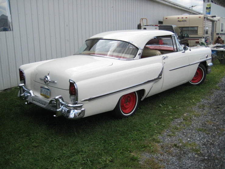 a vintage white car sitting in front of a garage