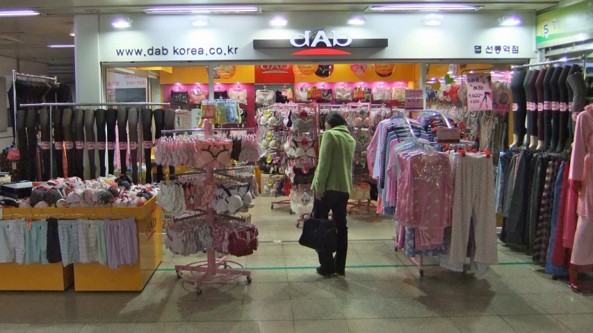 an asian woman standing in front of a store with lots of shirts on display