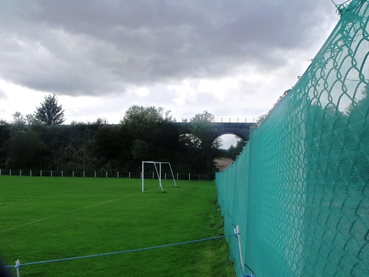 a field of grass with a fence and soccer goal in the background