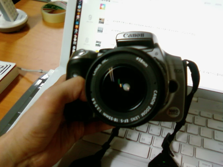 a person holding up an electronic camera next to a laptop computer