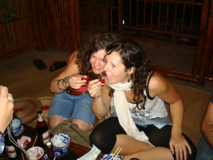 two women are sitting on the couch sharing a drink