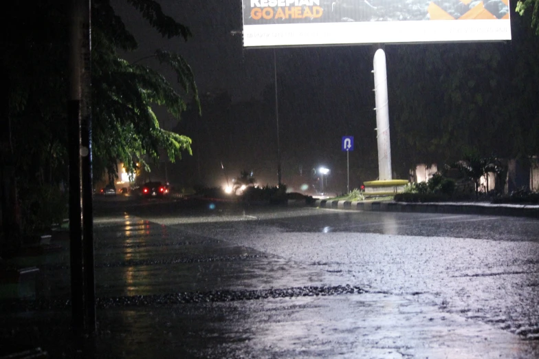 a city street is empty at night, and a large sign is in the background