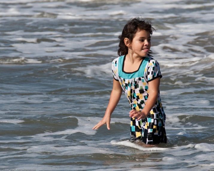 a child wearing a colorful patterned dress wading through the water