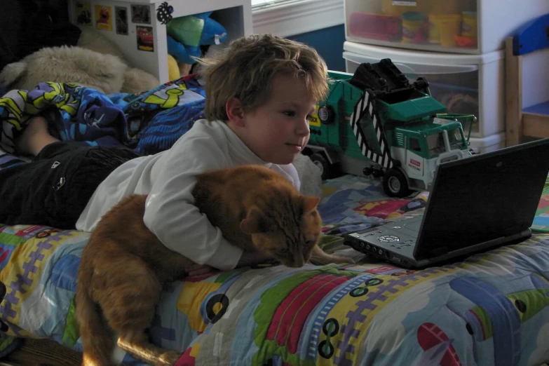 the small child has a cat in his lap as they sit on a bed