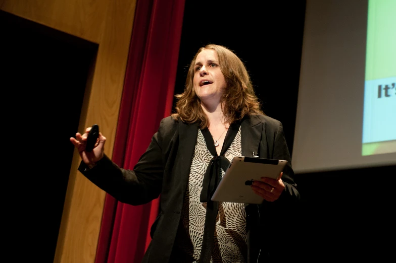 a woman in a black jacket is giving a lecture