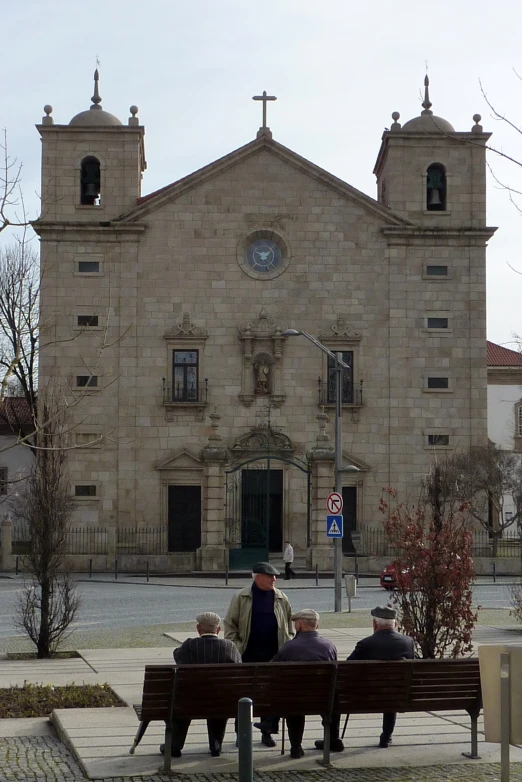 four people are sitting on a bench in front of a church