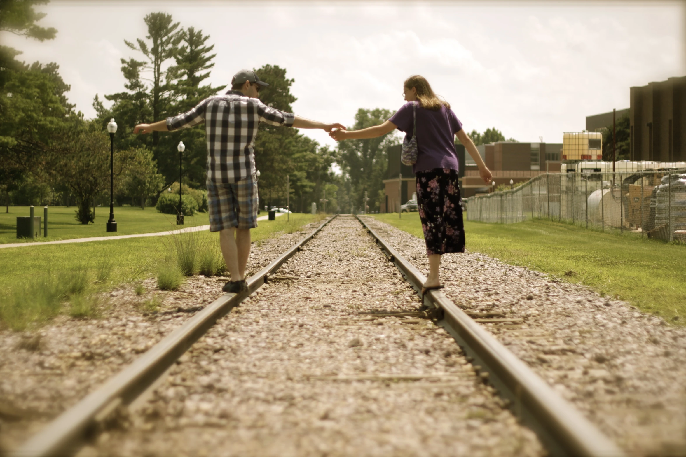 a man and woman hold hands on top of the railroad tracks