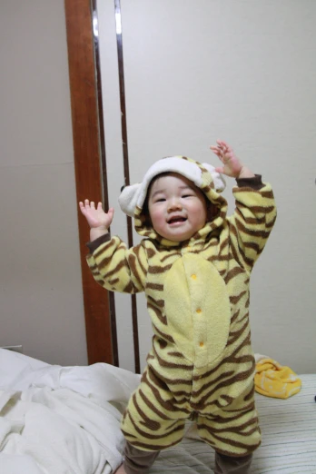 a baby with a lion suit on jumps on the bed