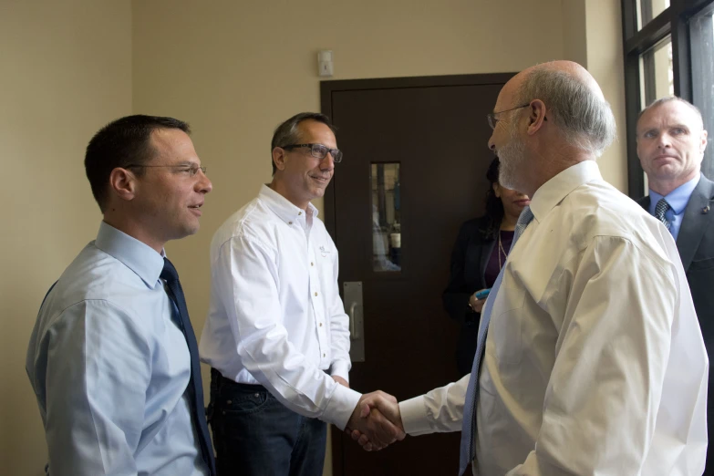 five men standing in a meeting room shaking hands