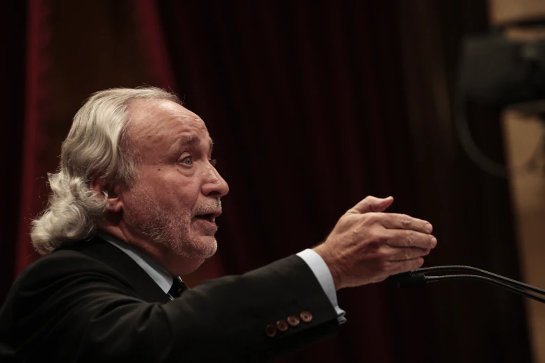 a man with white hair and long gray hair is giving a speech