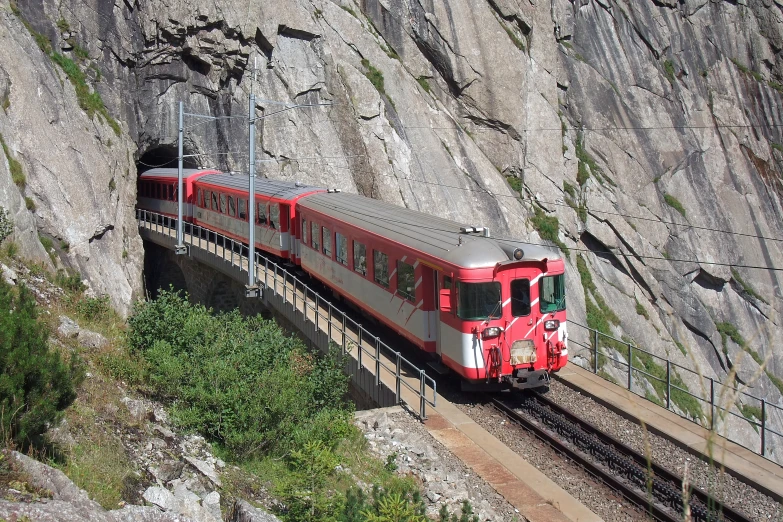 the train is travelling on the track beside mountains